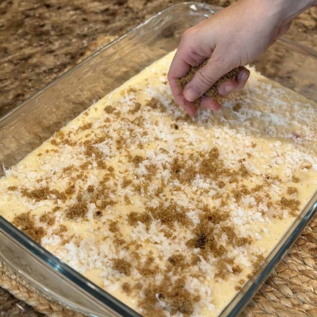 Sprinkling brown sugar and coconut on fruit cocktail cake batter in a pan.