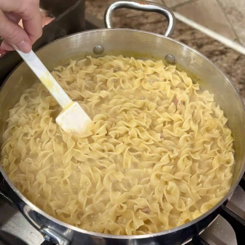 Stirring noodles in a skillet in soup.