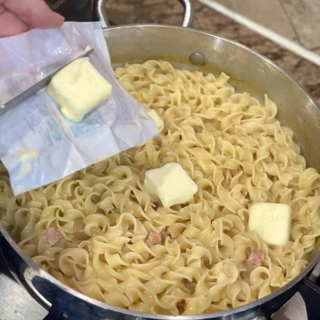 Adding butter to noodles in a pan.