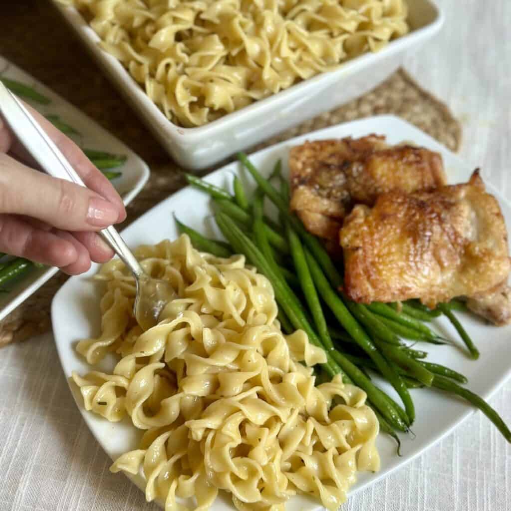 A plate of cafeteria noodles, green beans, and chicken. 