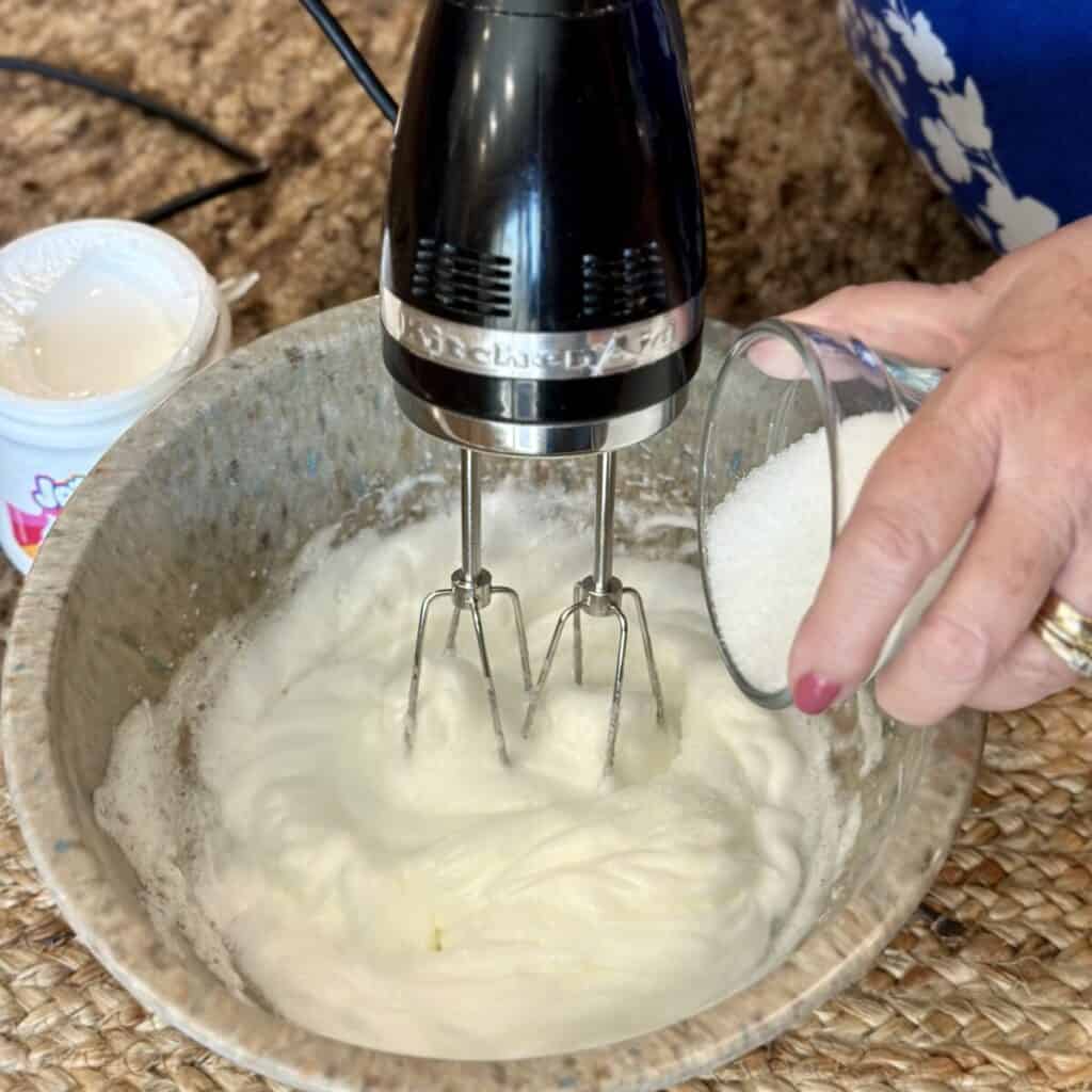 Adding sugar to egg whites in a bowl.