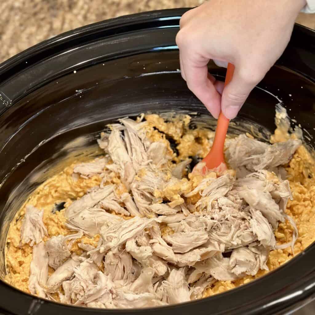 Adding chicken to slow cooker buffalo chicken dip in a slow cooker.