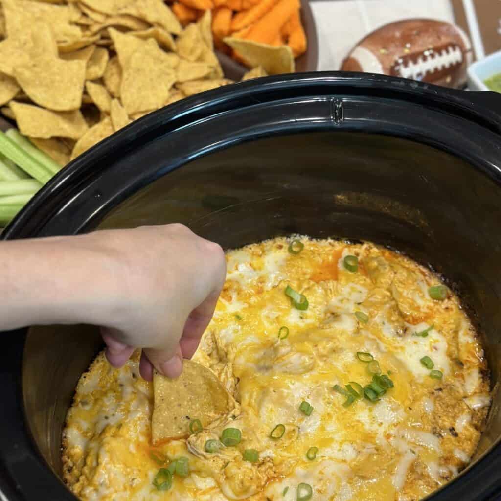 Dipping a chip into buffalo chicken dip in a slow cooker.