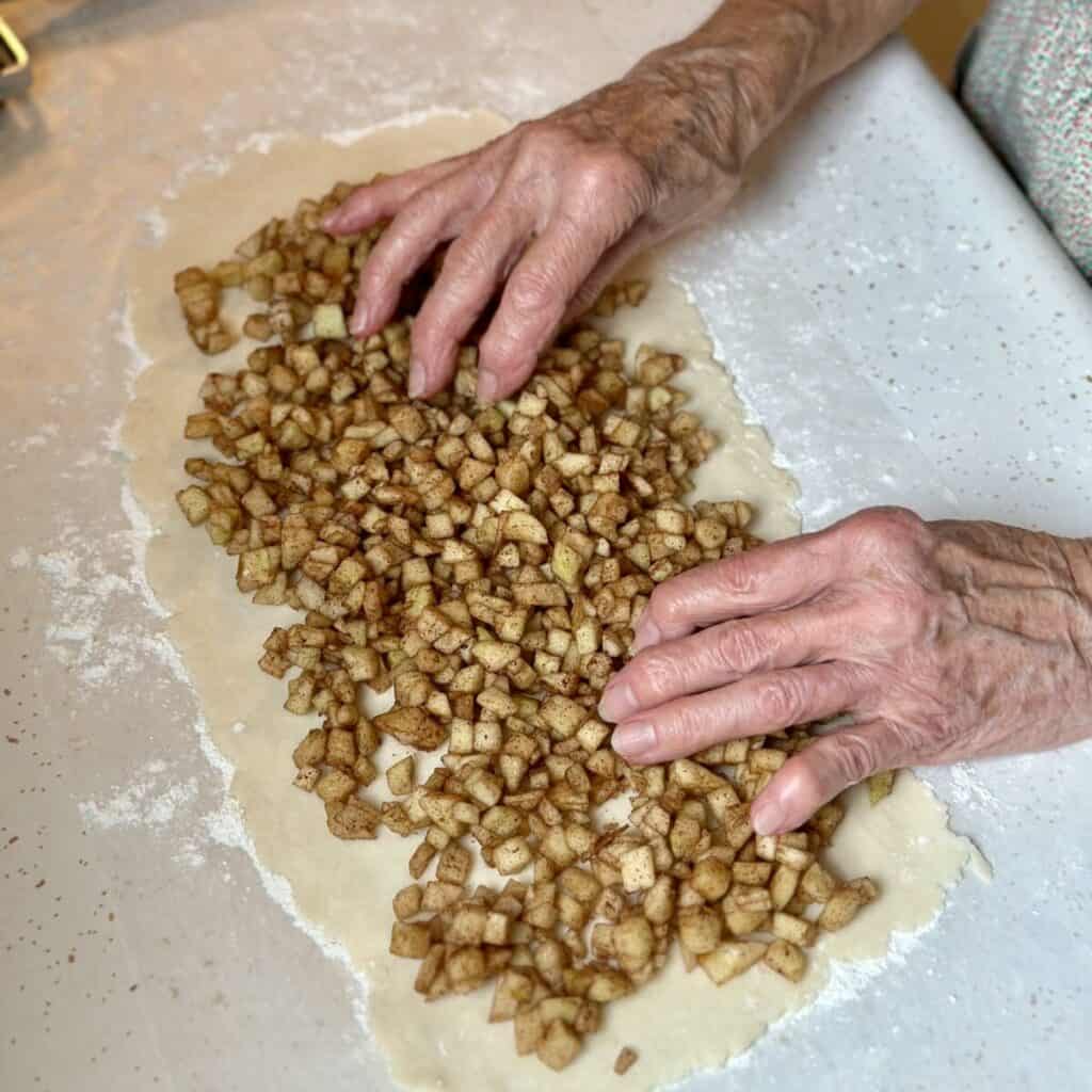 Spreading cinnamon apples on dough.