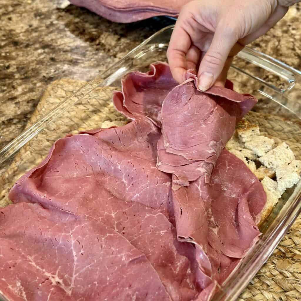 Adding corned beef to the top of a Reuben casserole.