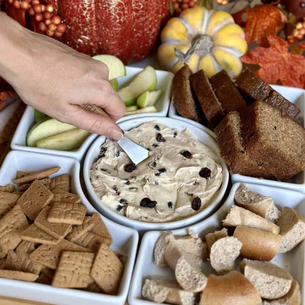 A tray of cinnamon cream cheese spread, apples, bread, crackers and bagels.