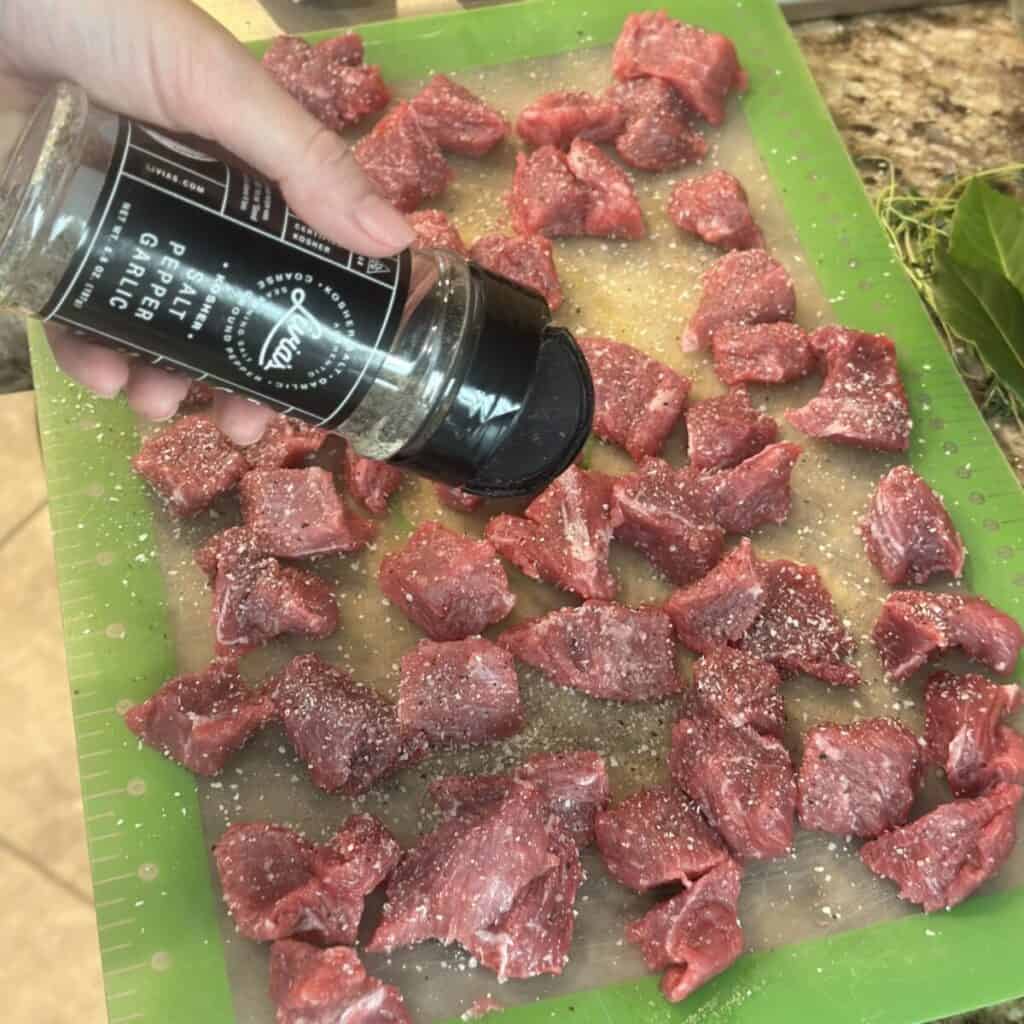 Seasoning beef chunks on a cutting board.