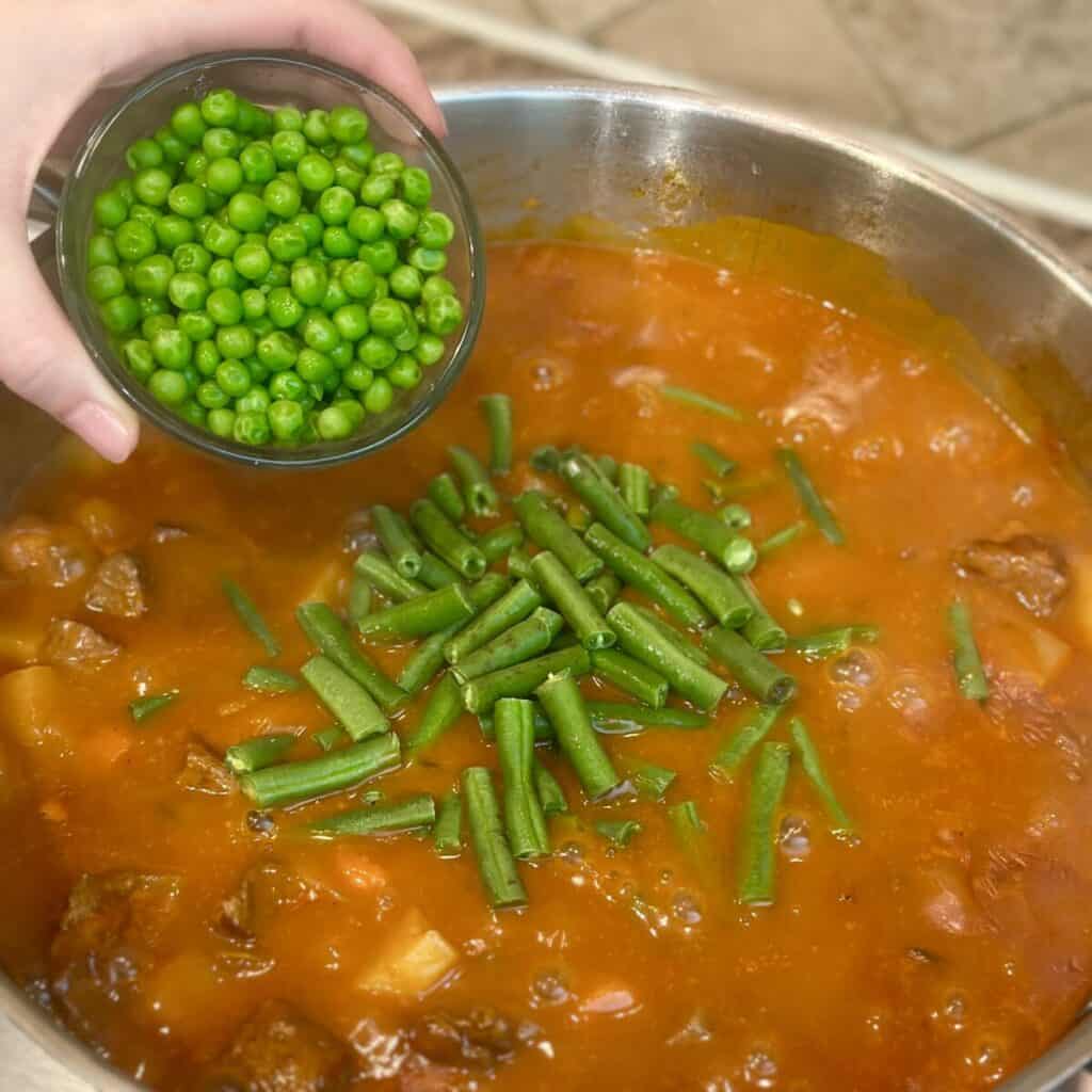 Adding green beans and peas to vegetable beef stew.