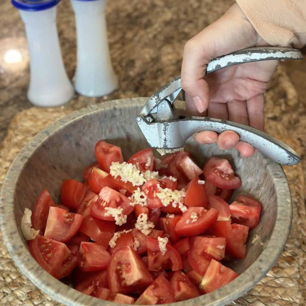 Adding garlic to tomatoes in a bowl.