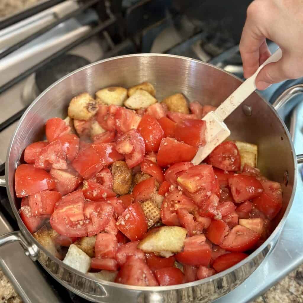 Mixing tomatoes and bread cubes in a pan.