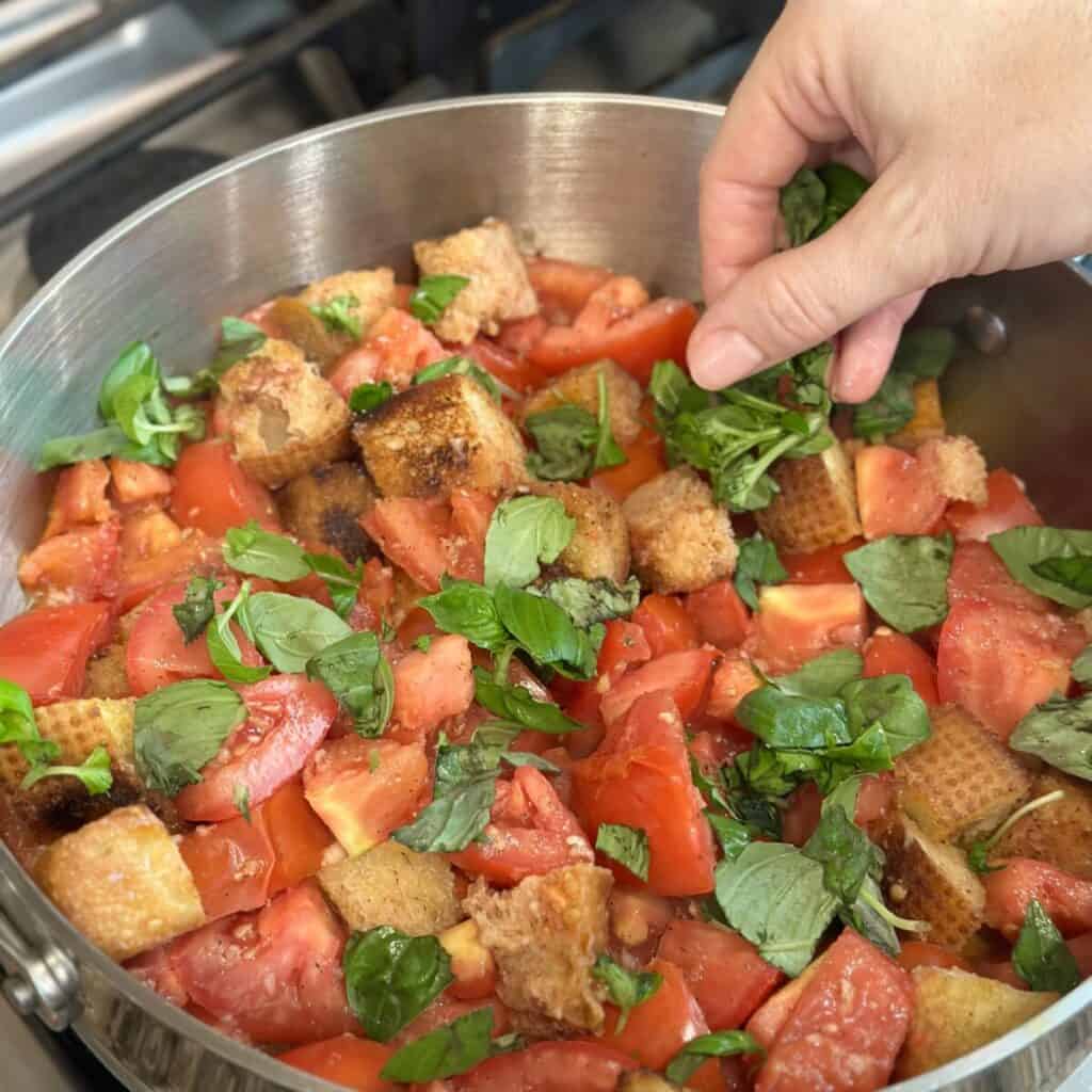 Adding basil to tomatoes in a pan.