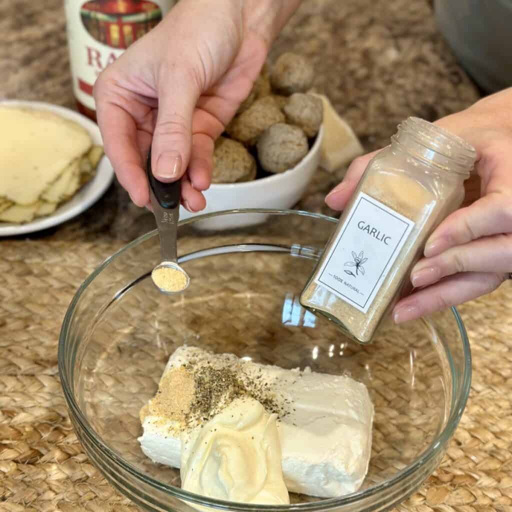 Making the cream cheese mixture in a bowl for meatball casserole.