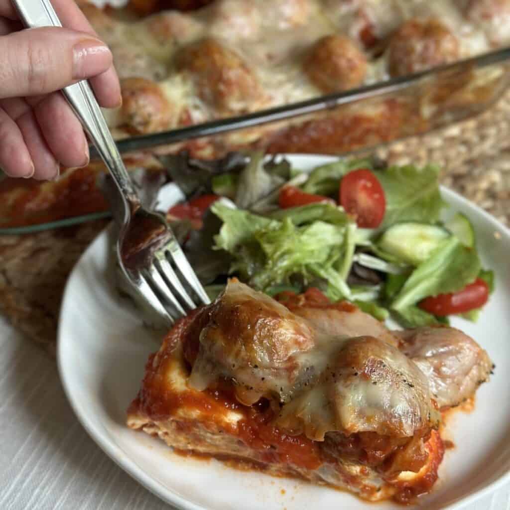 A serving of meatball casserole and salad on a plate.