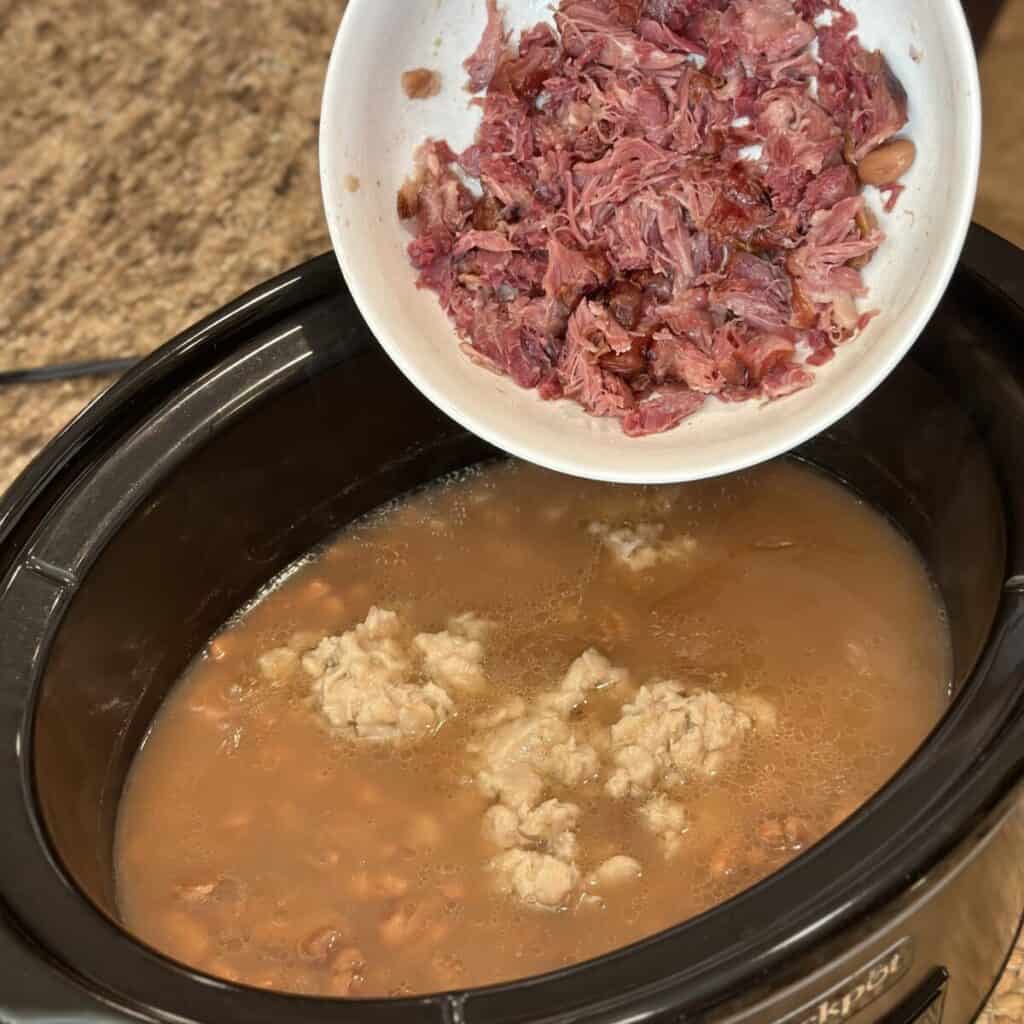 Adding smashed white beans and ham to pinto beans in a bowl.