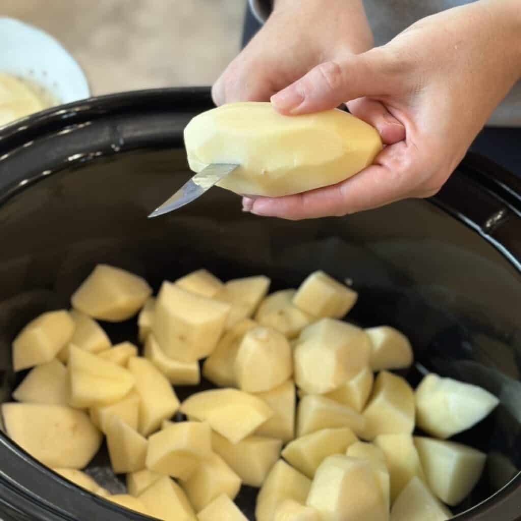 Slicing peeled potatoes into a crockpot.