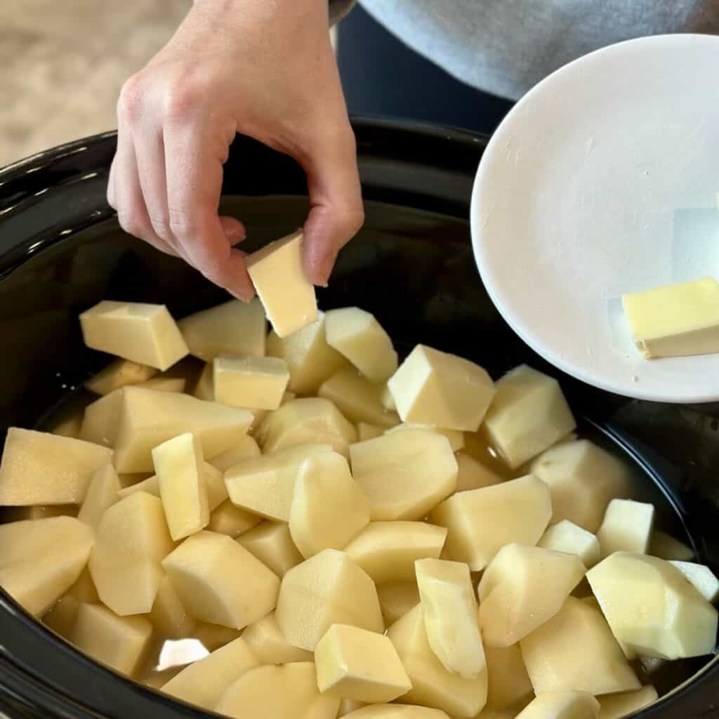 Adding butter to potatoes in a crockpot.