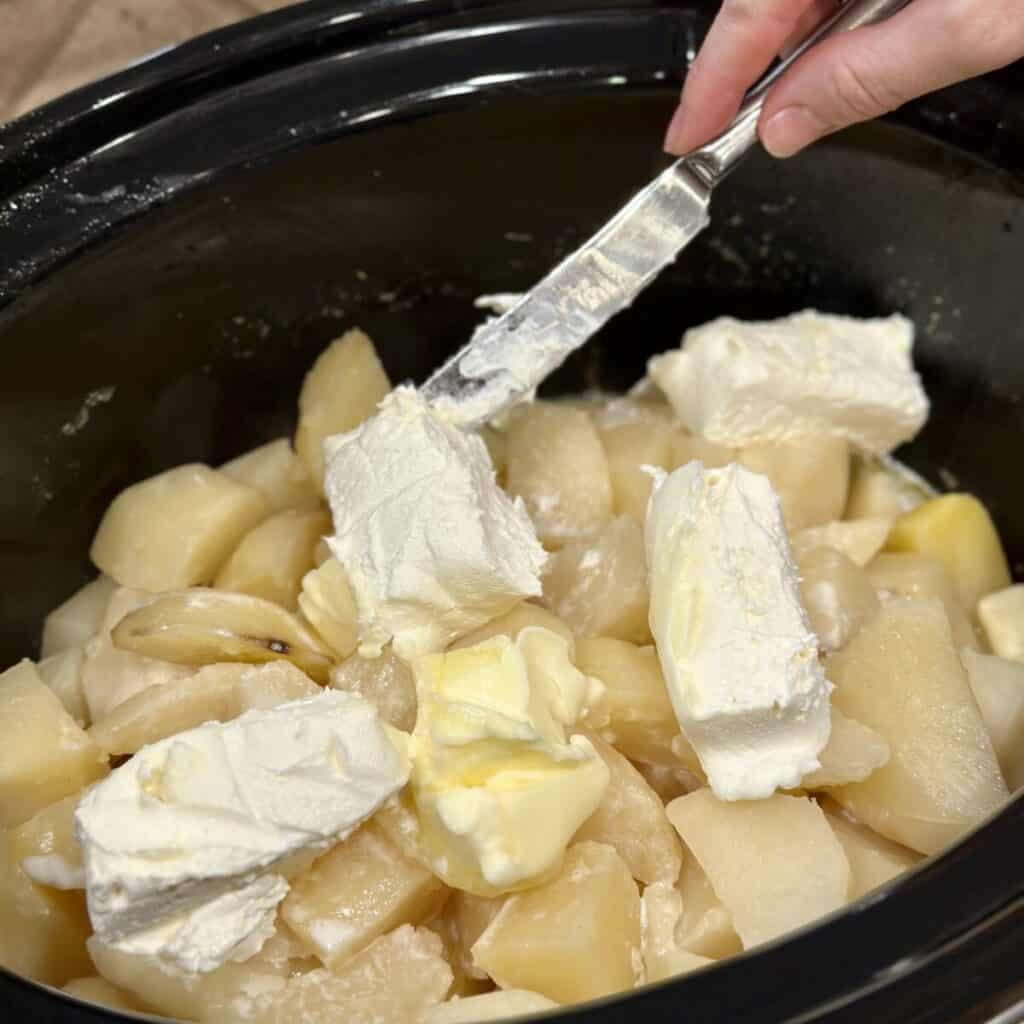 Adding cream cheese and butter to potatoes in a crockpot.