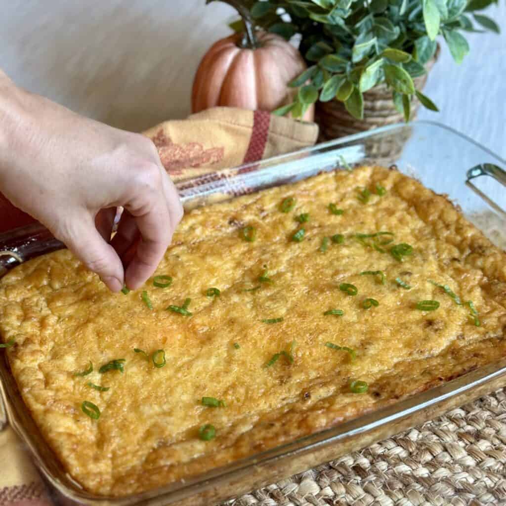 Adding green onions to the top of cooked cheesy grits.