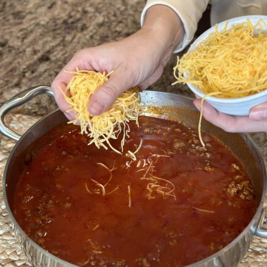 Adding cheese to chili in a skillet.