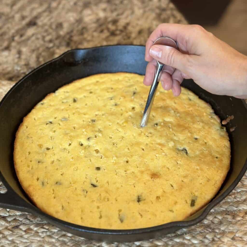 Poking holes in a baked pan of cornbread.