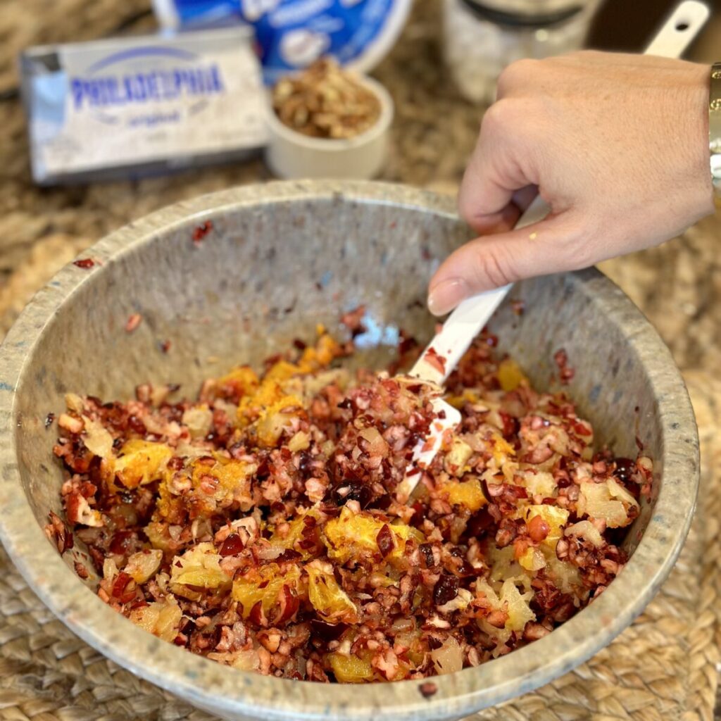 Mixing together pineapple, orange, cranberries and sugar in a bowl.