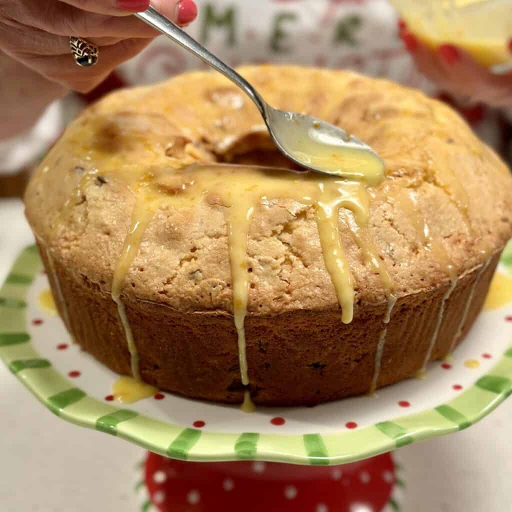 Adding glaze to the top of a cranberry orange pound cake.