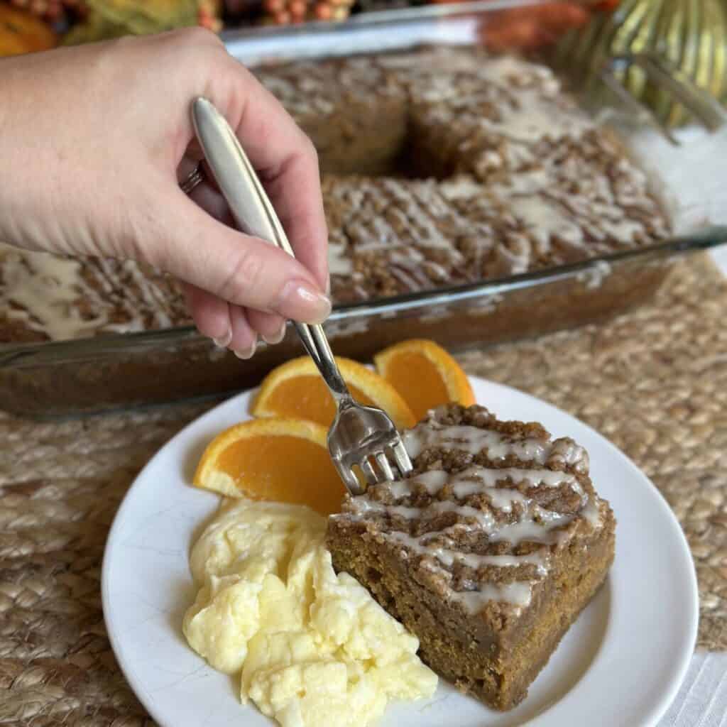 A slice of pumpkin coffee cake on a plate with eggs and orange slices.