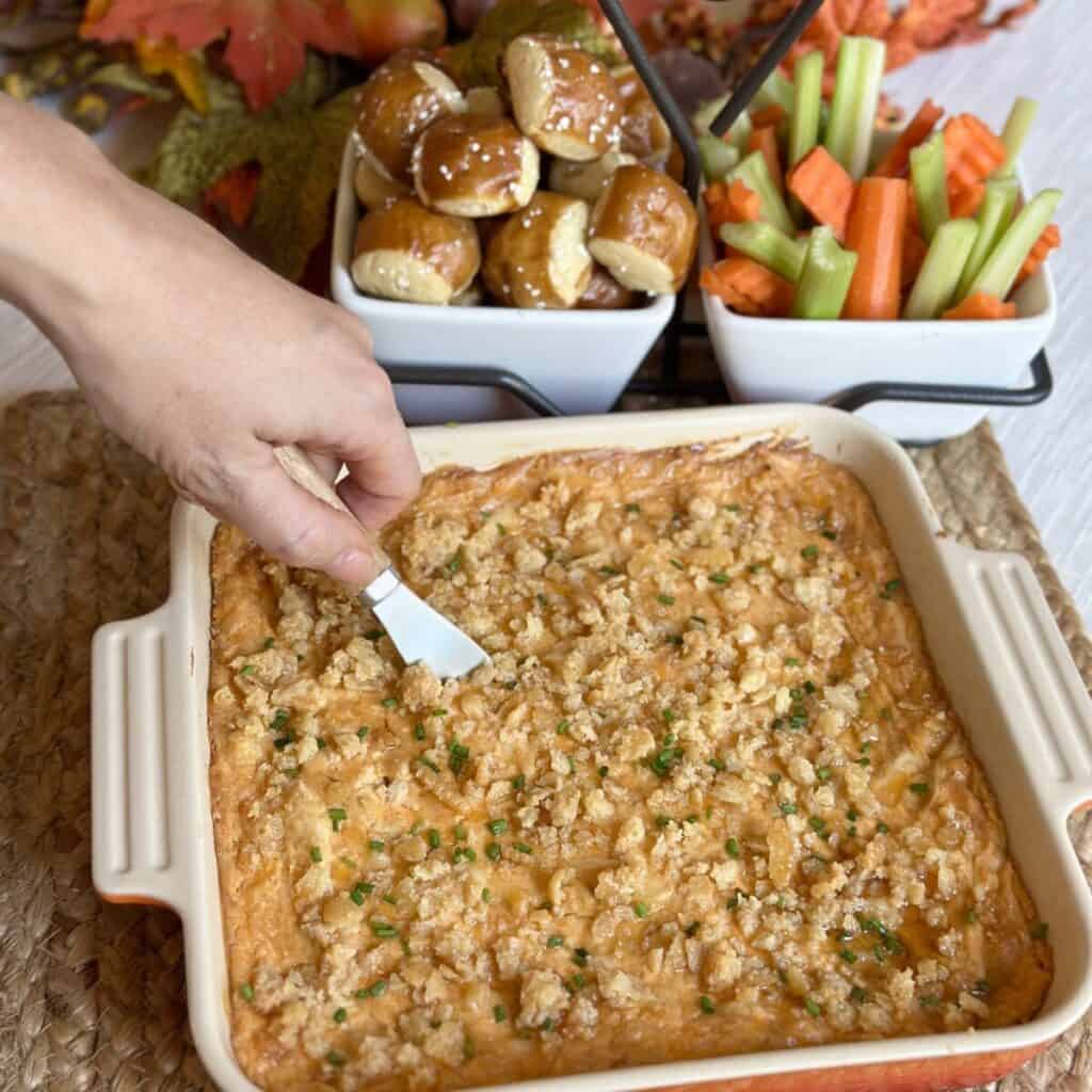 A baking dish of Nashville hot chicken dip and veggies and pretzels for dipping.