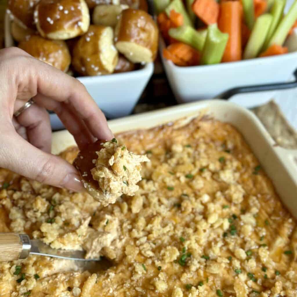 A baking dish of Nashville hot chicken dip and veggies and pretzels for dipping.