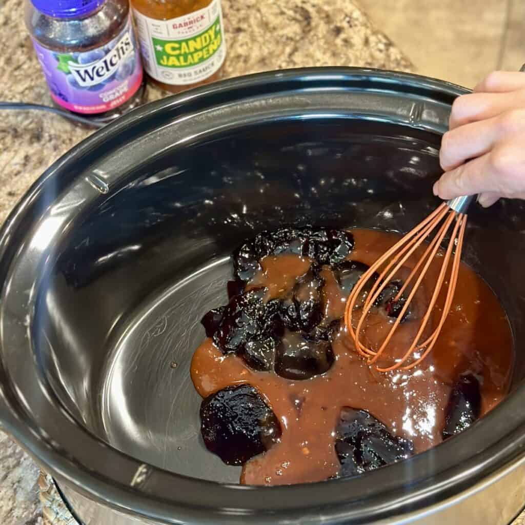 Whisking together bbq sauce and grape jelly in a crockpot.