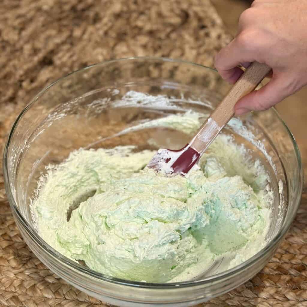 Mixing together cool whip and pistachio pudding in a bowl.