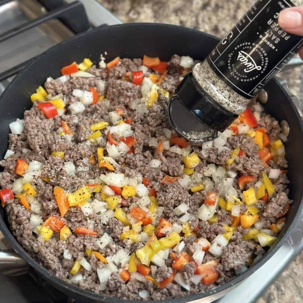 Seasoning ground beef with seasoning salt in a skillet.