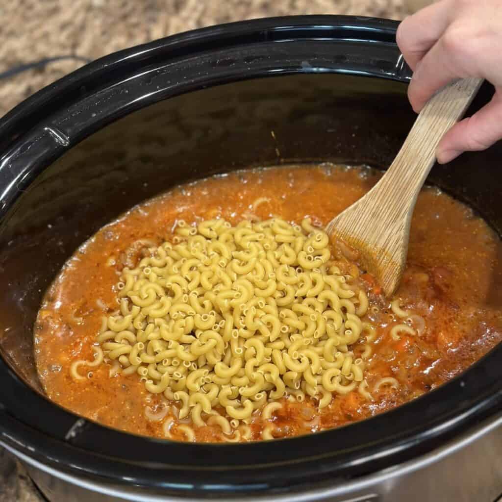 Adding pasta to a crockpot for slow cooker hamburger helper.